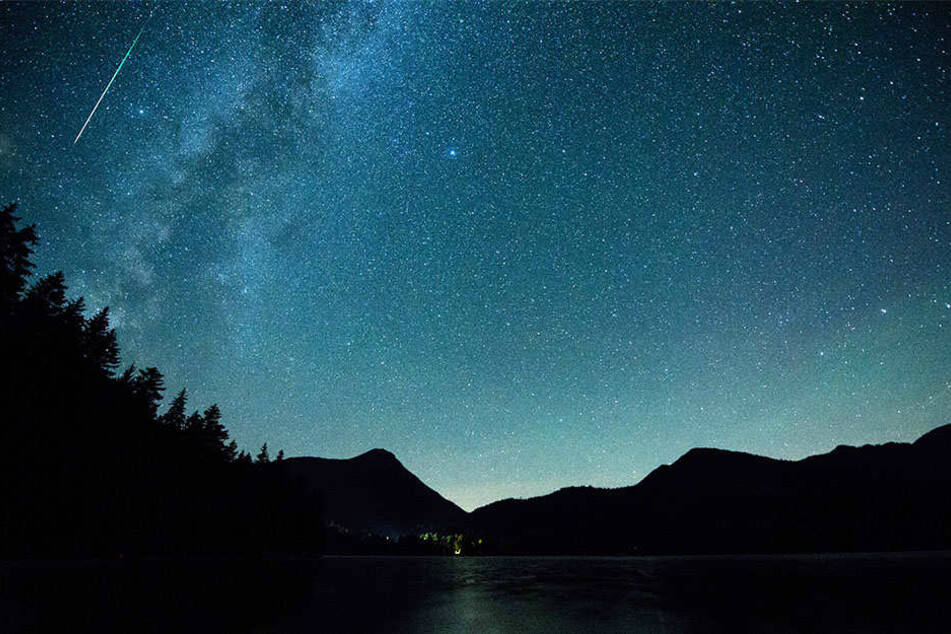 Eine Sternschnuppe leuchtet neben der Milchstraße am Himmel über dem Walchensee.