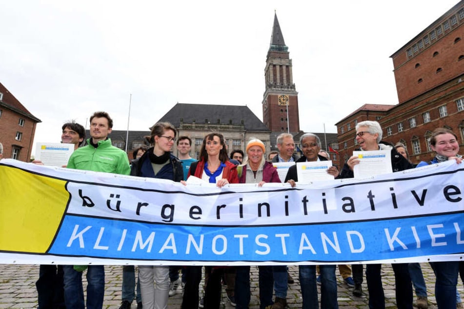 Mitglieder der Bürgerinitiative "Klimanotstand Kiel" stehen vor dem Rathaus. Die Bürgerinitiative stellte hier ihre Resolution mit Forderungen für die Landeshauptstadt Kiel zur Erklärung des Klimanotstands vor.