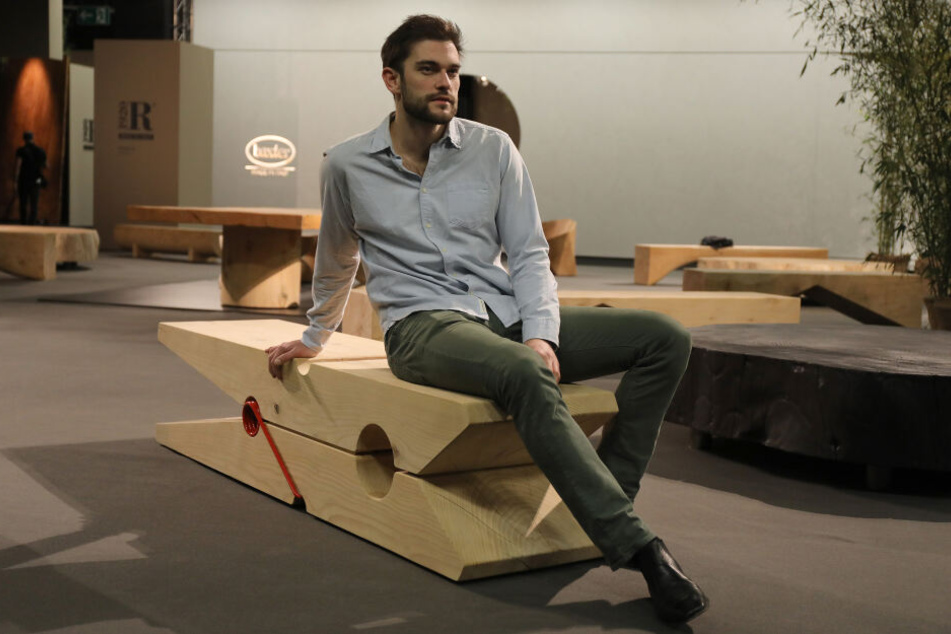 Ein Besucher sitzt auf einer Sitzgelegenheit aus Naturholz in Form einer Wäscheklammer (Hersteller: Made in Italy).
