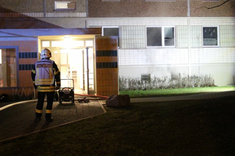 Ein Feuerwehrkamerad steht vor dem Hauseingang eines Plattenbaus in der Ludwigsburger Straße. Rechts neben ihm steigt Rauch aus dem Keller auf.