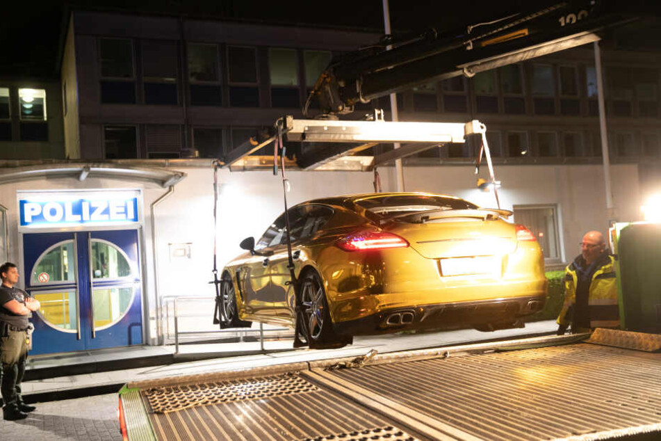 Ein Polizist steht vor einer Polizeiwache an einem mit Goldfolie beklebten Porsche Panamera, der auf einen Fahrzeugtransporter verladen wird.
