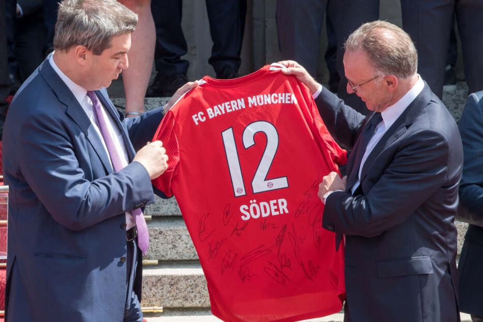 Karl-Heinz Rummenigge (2.v.l.), Vorsitzender des FC Bayern München, überreicht während eines Empfangs in der bayerischen Staatskanzlei Markus Söder (CSU), Ministerpräsident von Bayern, ein Fußball-Trikot mit der Nummer 12.