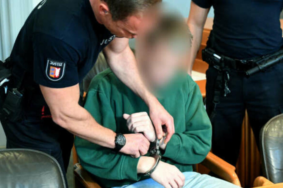 Ein Justizbeamter nimmt dem Angeklagten die Handschellen ab.