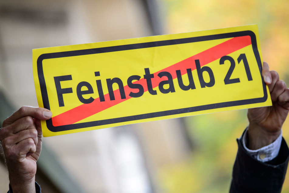 Ein Mann hält in Stuttgart vor dem Amtssitz von Ministerpräsident Kretschmann ein Schild mit der Aufschrift "Feinstaub 21 (durchgestrichen) hoch. (Archivbild)