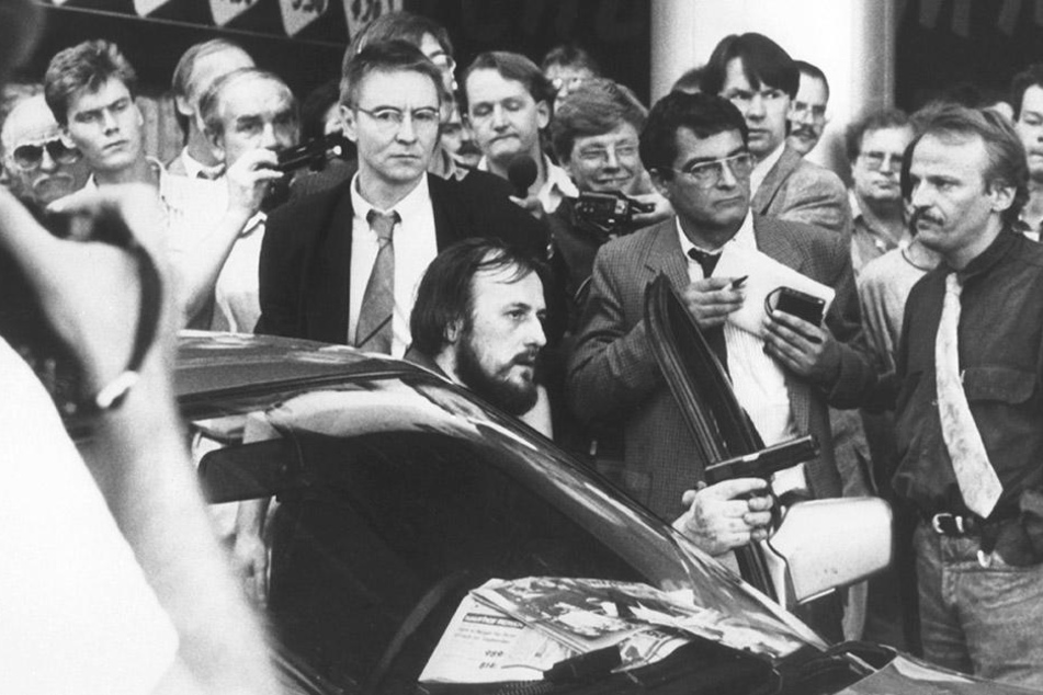 Mit einer Waffe in der Hand fordert der am Steuer des Fluchtfahrzeugs sitzende Hans-Jürgen Rösner am 18.08.1988 in der Innenstadt von Köln die umstehenden Journalisten und Passanten auf, den Weg frei zu machen.