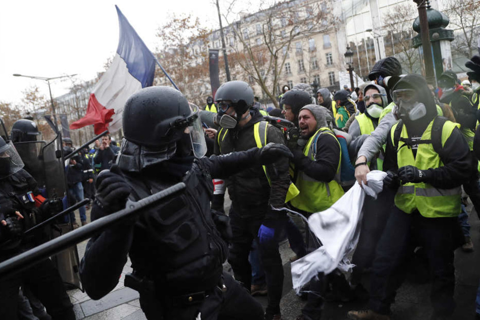 In Paris setzt ein Polizist einen Schlagstock gegen Demonstranten der "Gilets Jaunes" (Gelbwesten) ein.