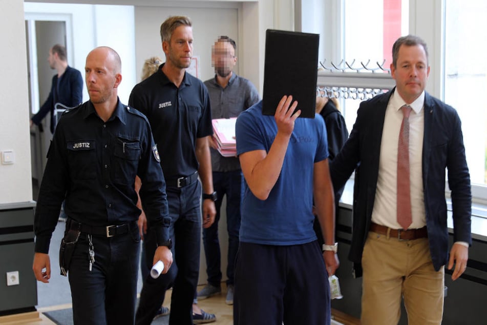 Einer der Angeklagten wird von zwei Beamten und seinem Anwalt (rechts) in den Gerichtssaal geführt.