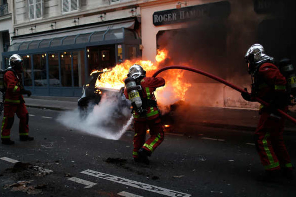 Feuerwehrleute löschen während der Proteste und Ausschreitungen der "Gelbwesten" in Paris ein brennendes Auto.
