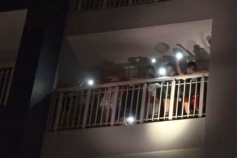 Bewohner eines Wohnkomplexes rufen mit den Lichtern ihrer Mobiltelefone um Hilfe nach dem Aubruch eines Feuers.