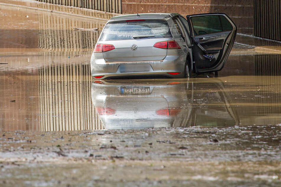 Ein Auto ist im Wasser stecken geblieben. Die komplette Straße ist in Schlamm getränkt.