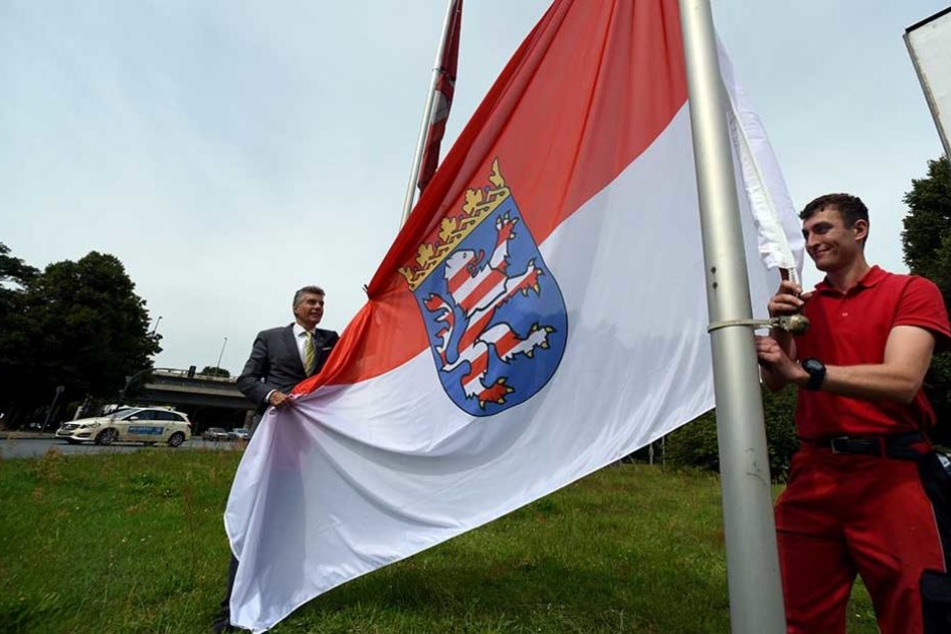 Der stellvertretende Bezirksbürgermeister Carsten Engelmann (l) und der Mitarbeiter des Bezirks, Stephan Böttcher hissen die hessische Fahne am Jakob-Kaiser-Platz.