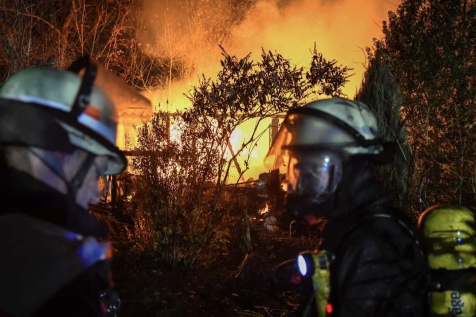 Zwei Feuerwehrleute stehen vor der brennenden Gartenlaube.
