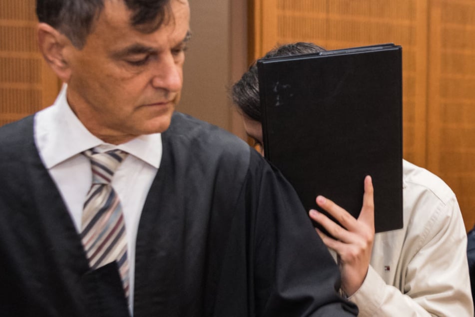 Der 27-jährige Angeklagte hält sich eine Mappe vor das Gesicht.