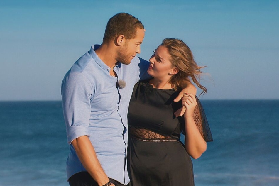 Ernestine und Andrej laufen Arm in Arm den Strand entlang.