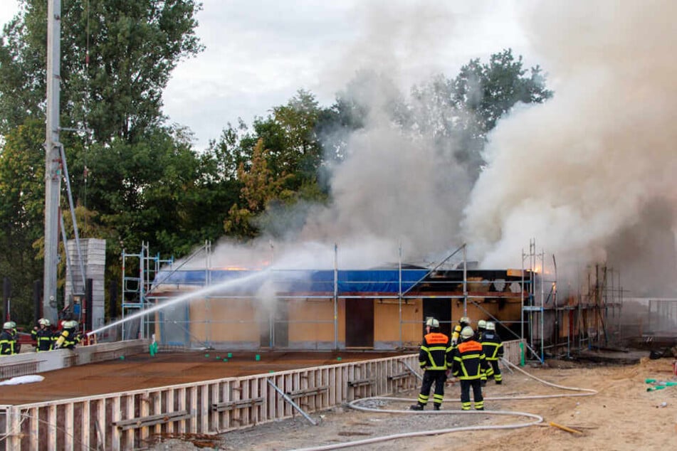 Feuerwehrleute löschen mit Wasser den brennenden Rohbau.