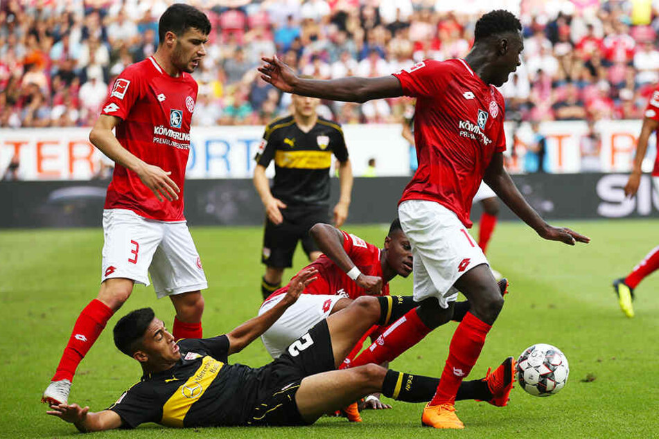 VfB-Stürmer Nicolas Gonzalez (M.) grätscht in den Mainzer Moussa Niakhate (r.) rein. Aaron Martin (l.) und Ridle Baku (Mitte-hinten) schauen zu.