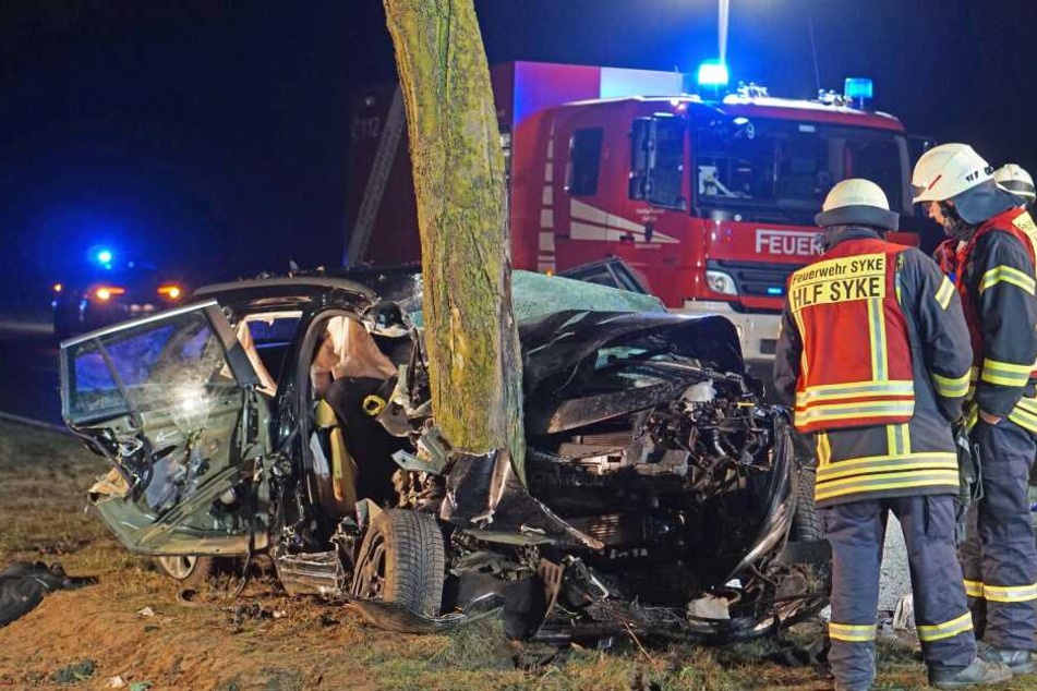 Einsatzkräfte der Feuerwehr stehen neben dem Wrack des Autos.