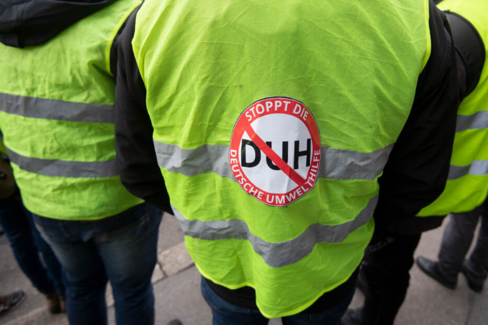 An seiner gelben Weste hat ein Demonstrant einen Aufkleber mit "Stoppt die Deutsche Umwelthilfe" kleben.