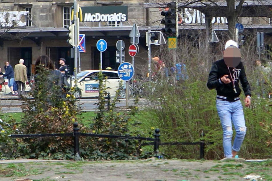Mit etwas in der Hand verlässt der junge Mann die Rabatte und eilt auf die andere Wegseite zu einem Busch.