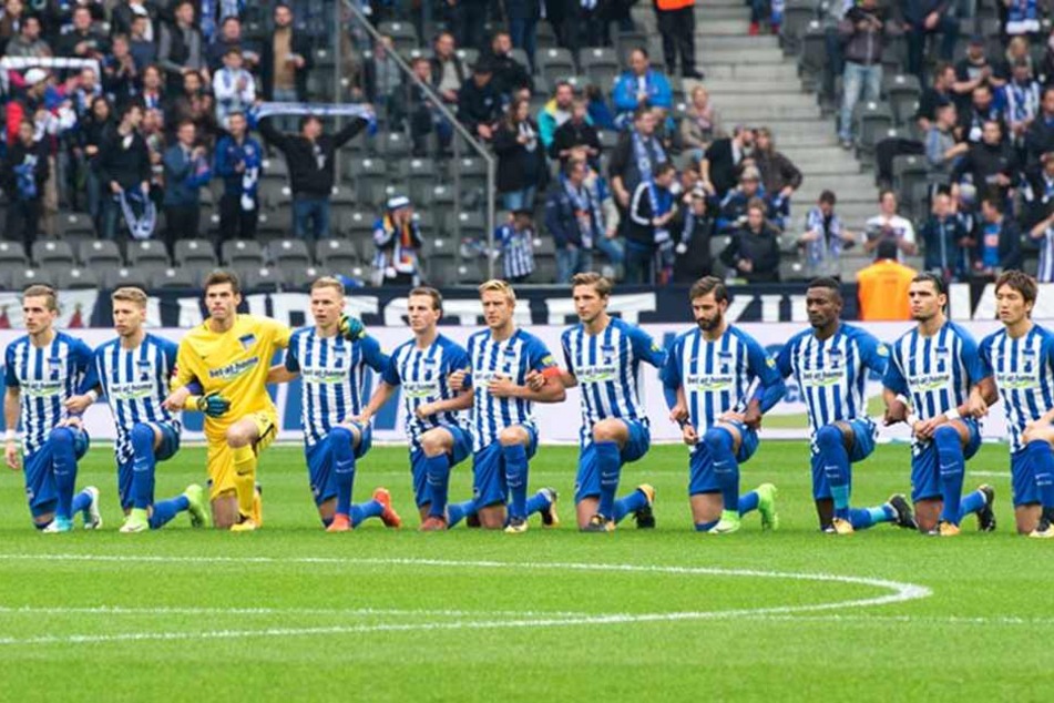 Die Spieler von Hertha BSC knien vor dem Anpfiff auf dem Rasen.