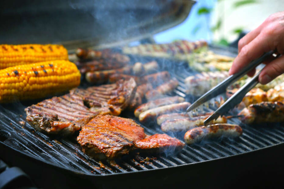 Maiskolben, Fleischspieße, Bratwürste und Steaks liegen auf dem Rost eines Gasgrills.