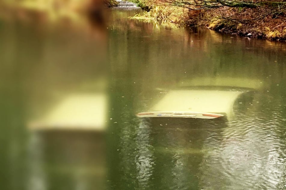 Ein Auto steht mit geöffnetem Kofferraum auf dem Grund eines Teiches.