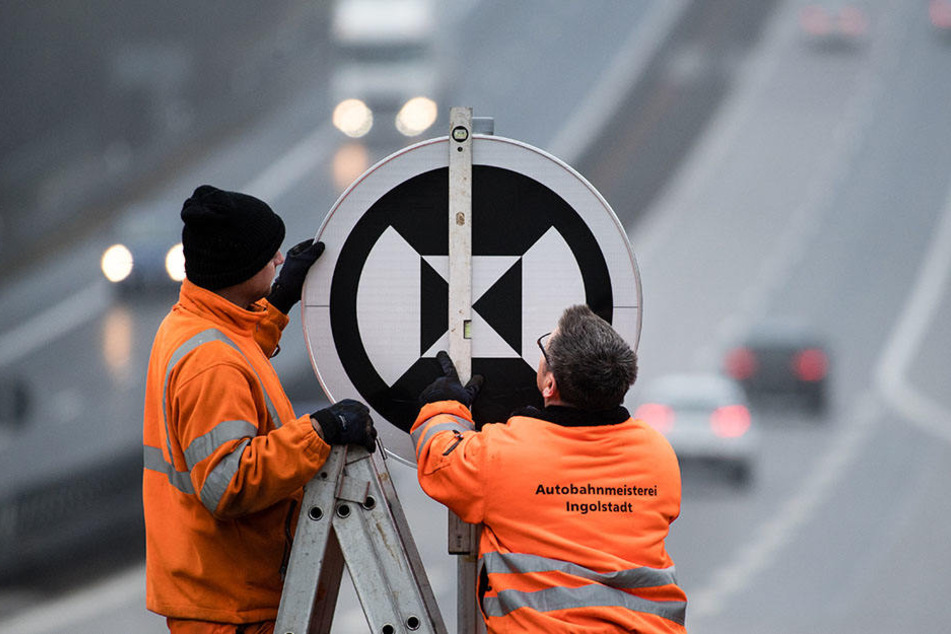 Zwei Mitarbeiter der Autobahnmeisterei stellen ein neues Verkehrsschild auf.