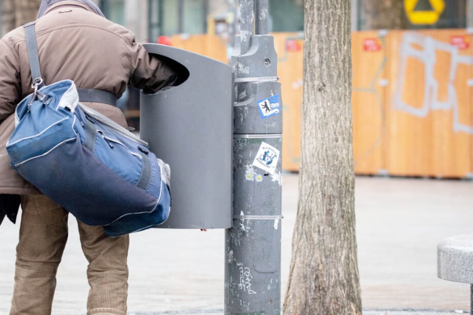 Ein Mann sucht in einem Mülleimer nach Pfandflaschen.