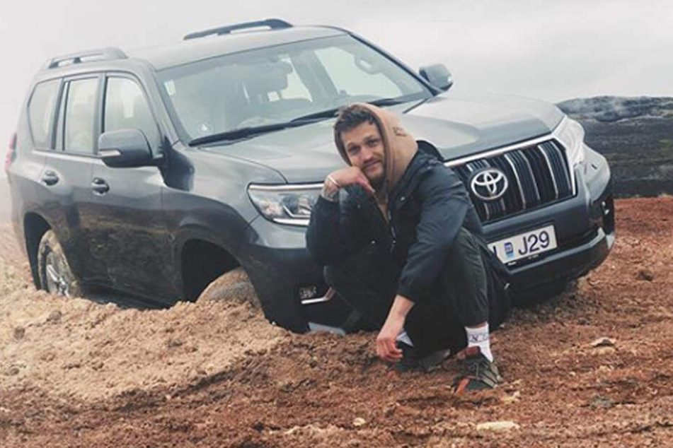 Alexander Tikhomirov posiert lächelnd vor seinem verunglückten Wagen.