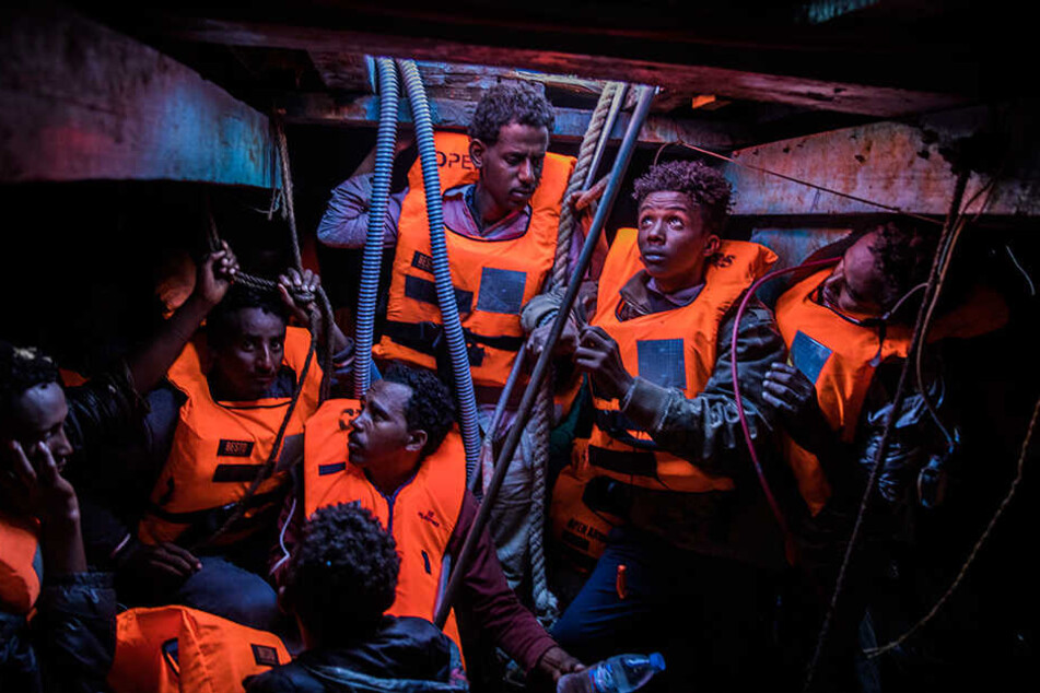 Mehrere Flüchtlinge aus verschiedenen afrikanischen Ländern sitzen an der Küste zu Libyen im unteren Bereich eines überfüllten Holzbootes und warten auf Rettung.