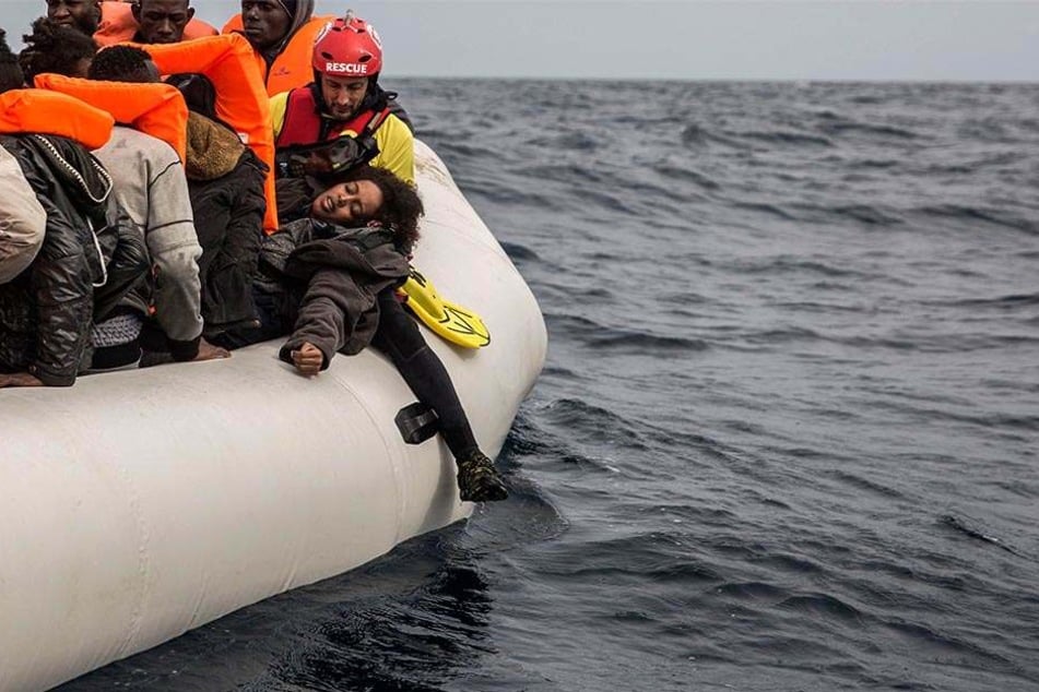 18.02.2018, Mittelmeer: Eine Frau liegt erschöpft in den Armen eines Mitarbeiters der spanischen Menschenrechtsorganisation Proactiva Open Arms auf einem überfüllten Rettungsboot nördlich von Al-Khums (Libyen).