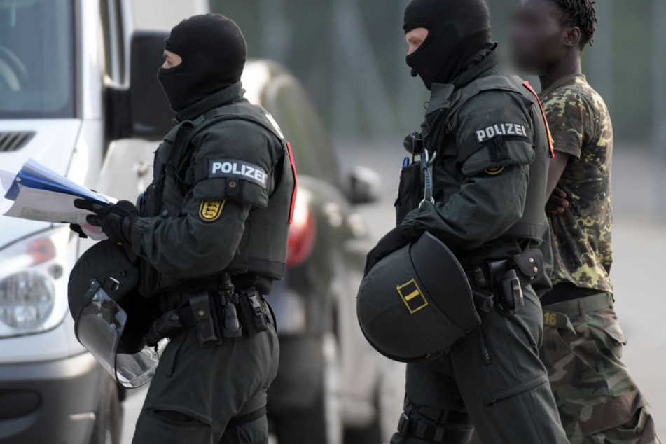 In der Landeserstaufnahmeeinrichtung für Flüchtlinge (LEA) in Ellwangen wird ein Mann von maskierten Polizisten eskortiert. (Archivbild)