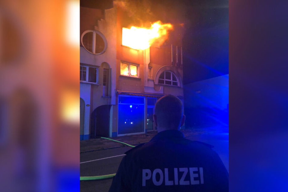 Ein Polizist steht vor dem Wohnhaus, aus dem meterhohe Flammen schlagen.