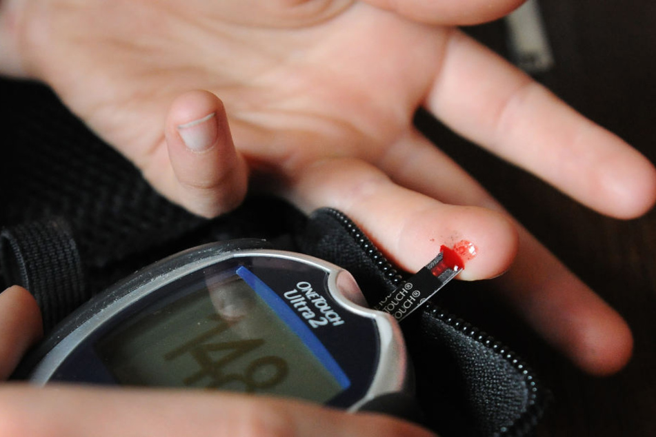Ein Mädchen, das an Diabetes Typ 1 erkrankt ist, misst mit einem Blutzuckermeßgerät ihren aktuellen Zuckergehalt im Blut.