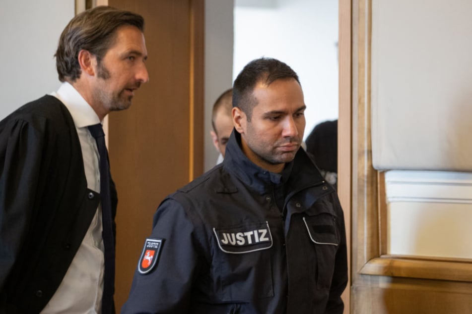 Verteidiger Frank Otten (l) blickt auf seinen Mandanten (2.v.r, verdeckt) der von Justizbeamten in den Gerichtssaal geführt wird.