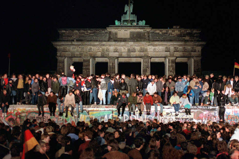 Jubelnde Menschen stehen auf der Berliner Mauer am Brandenburger Tor am. Die BerlinerMauer stand 28 Jahre, 2 Monate und 26 Tage.