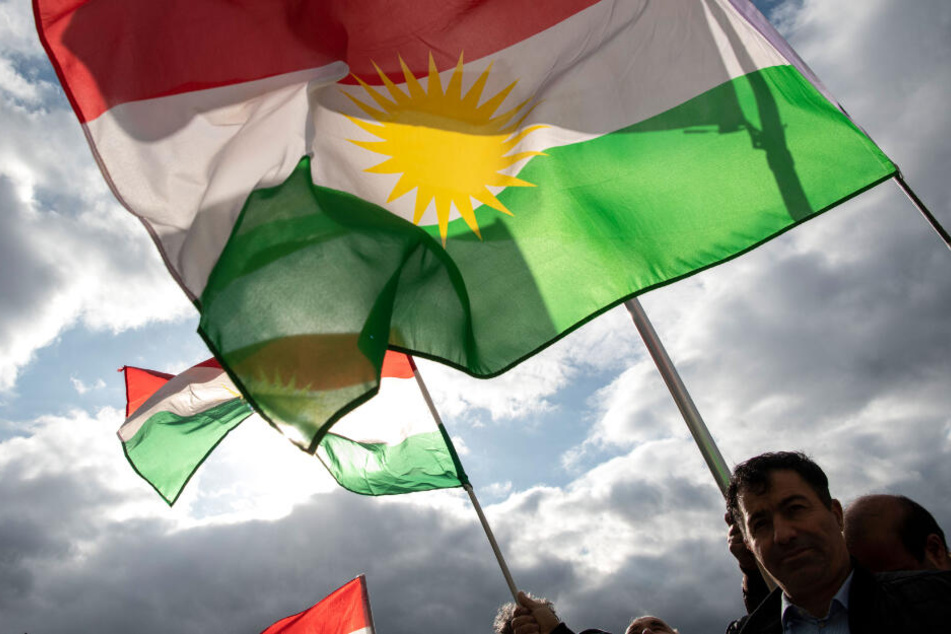 Demonstranten halten bei einer Protestaktion gegen die türkische Militäroffensive in Nordsyrien am Pariser Platz Fahnen der Autonomen Region Kurdistan.