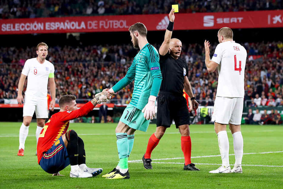 ...und bekommt dafür vom polnischen Schiedsrichter Szymon Marciniak (Zweiter von rechts) die Gelbe Karte, während Spaniens Keeper David de Gea (Vorne, Zweiter von links) Sergio Ramos (Vorne, Erster von links) aufhilft.