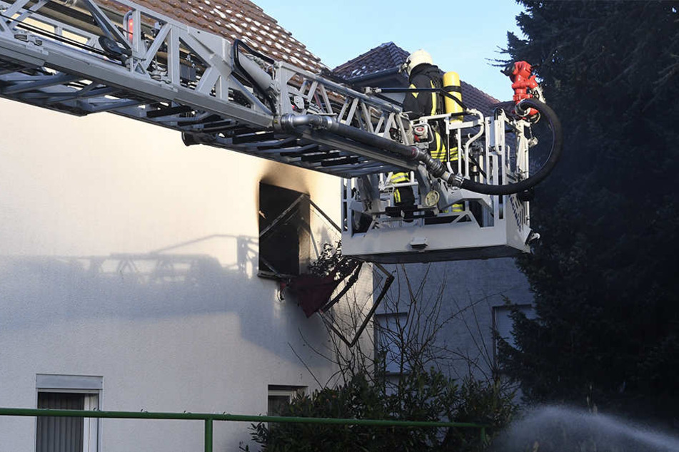 Feuerwehrleute bringen ein ausgebranntes Bettgestell ins Freie.