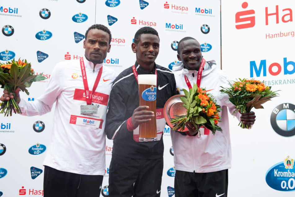 Marathon-Sieger Tadu Abate (Mitte) aus Äthiopien jubelt beim 34. Hamburg Marathon bei der Siegerehrung, links steht der zweitplatzierte Ayele Abshero aus Äthiopien und rechts der drittplatzierte Stephen Kiprotich aus Uganda.