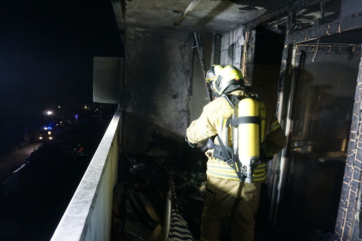 Ein Feuerwehrmann steht auf dem Balkon der ausgebrannten Wohnung.