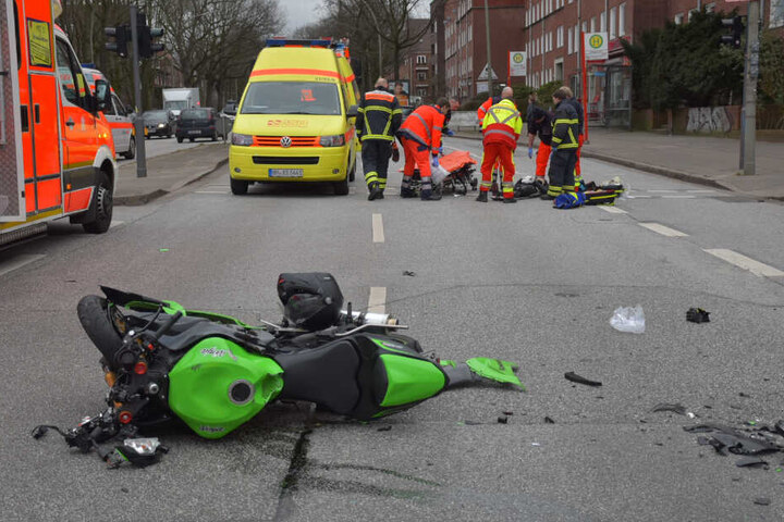 Das Motorrad ist nach dem Unfall deutlich beschädigt. Rettungskräfte transportieren eine Person ab.