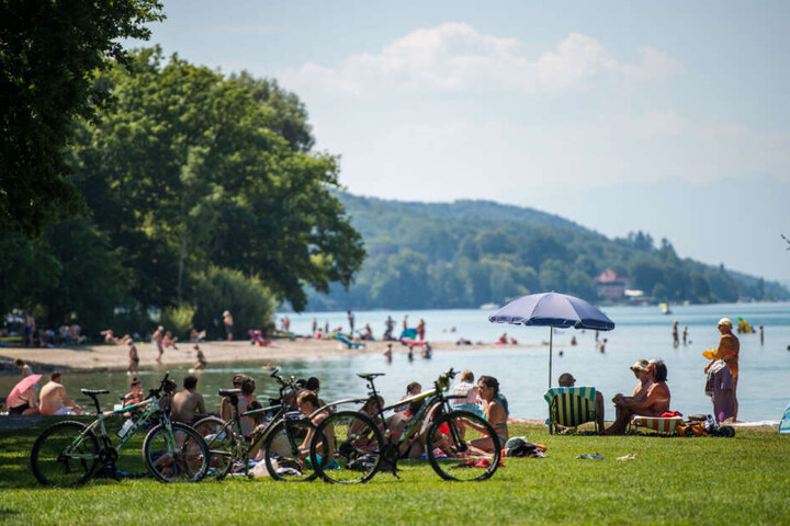 Badegäste liegen am Starnberger See an einem Strand.