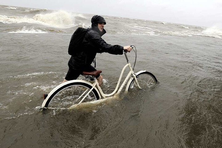 Tyler Holland schiebt sein Fahrrad durch Wasser, das durch Tropensturm "Barry" aus dem Lake Pontchartrain über den Damm geschoben wurde.