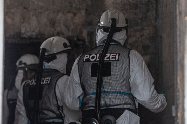 Kriminaltechniker in Atemschutzkleidung begutachten im ausgebrannten Haus ein Zimmer.