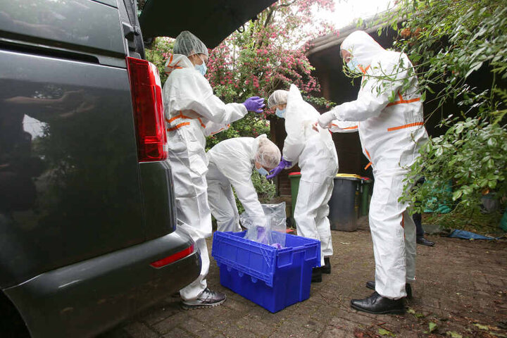 Ermittler der Mordkommsion stehen in weißen Schutzanzügen vor einem Haus, in dem zuvor ein Mann erschossen wurde.