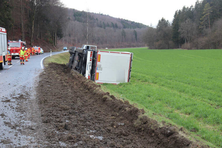 Rettungskräfte am Unfallort, wo ein Lkw auf der Seite in einer Böschung liegt.