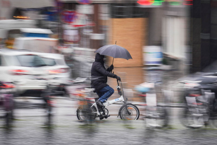 Ein Radler schützt sich während der Fahrt durch Frankfurt mit einem Schirm vor der Nässe.