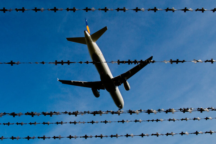 Ein Flugzeug fliegt über einen Stacheldrahtzaun. (Symbolbild)