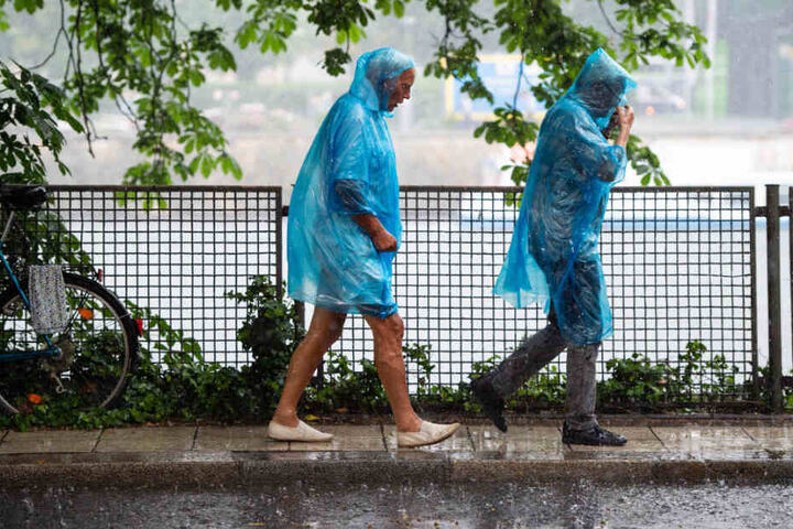 Eine Frau und ein Mann laufen in blauen Regencapes durch den Regen.
